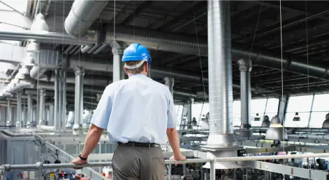 Hombre mirando planta de producción con casco azul y ropa de oficinista
