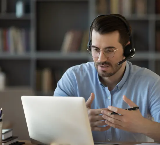 hombre joven con lentes y barba con audífonos y micrófono teniendo una video llamada en notebook